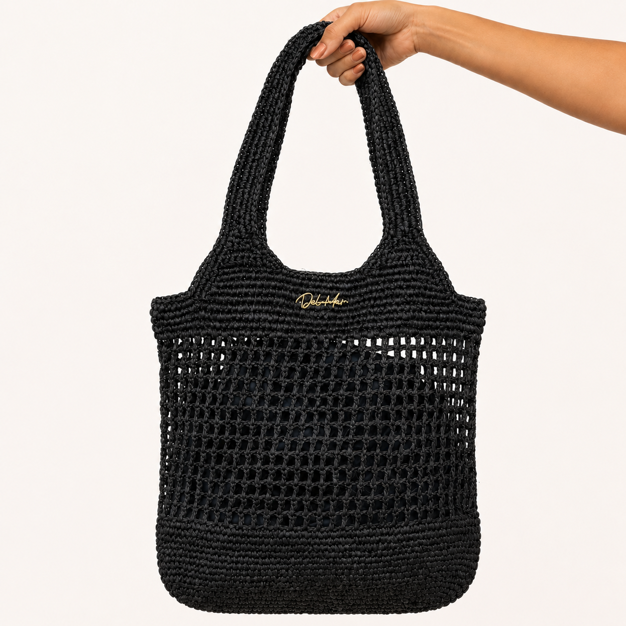 Black woven tote bag held by a hand on a white background