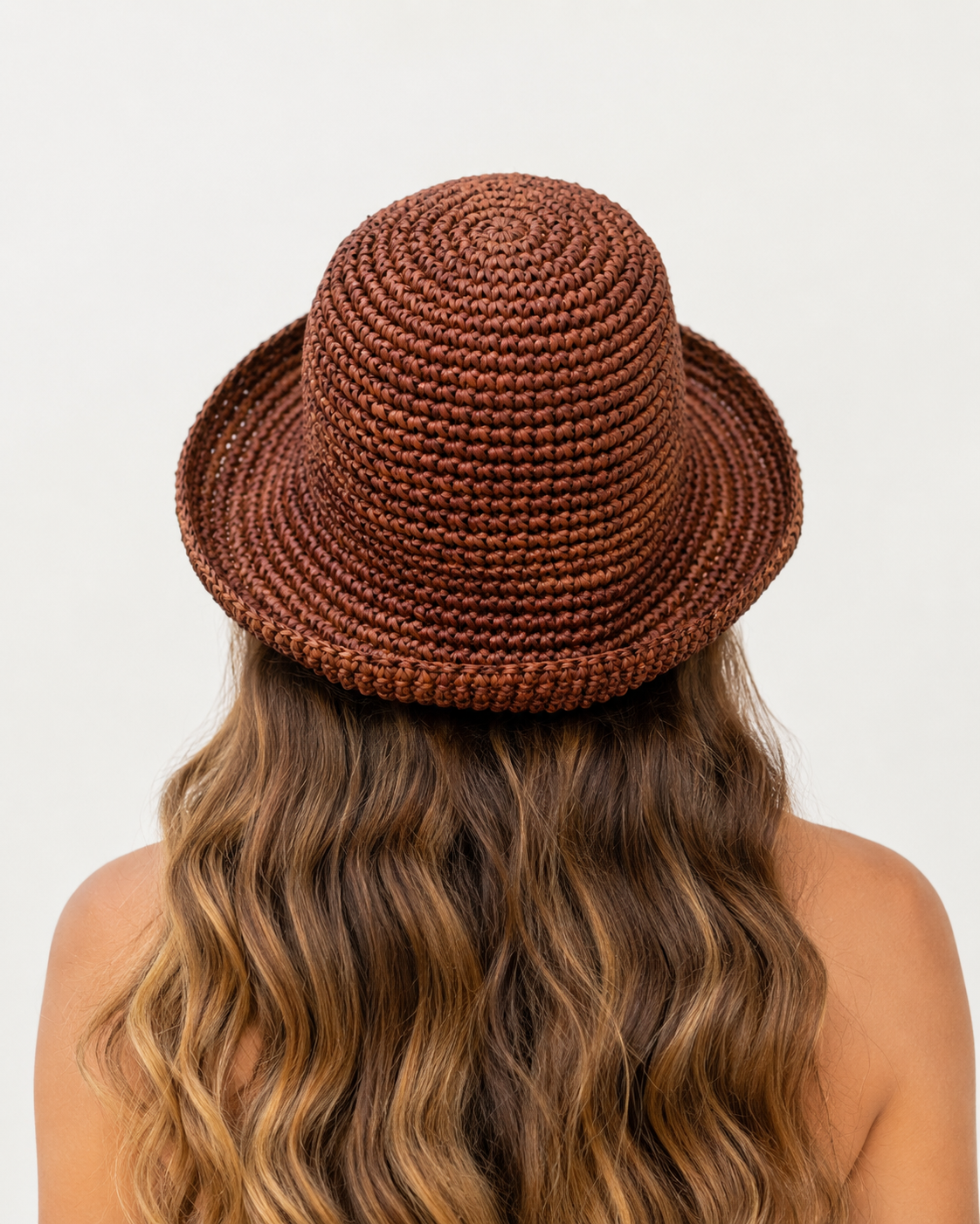 Brown woven hat worn by a person with long wavy hair on a light gray background