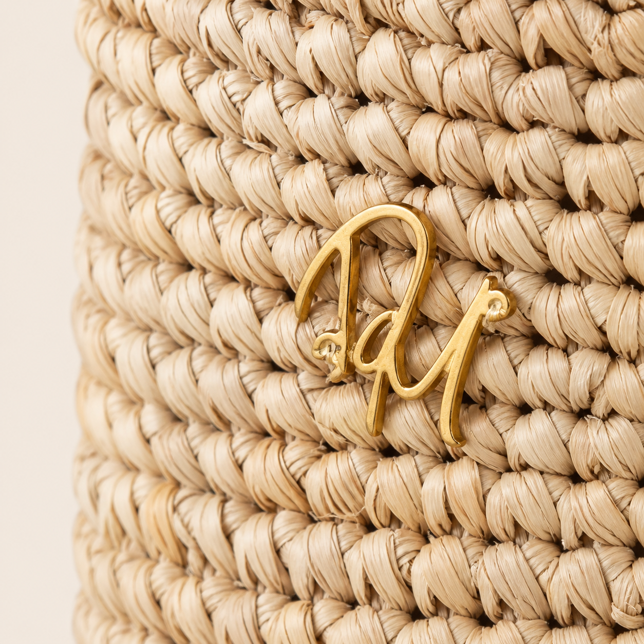 Gold jewelry with a logo on a woven beige background