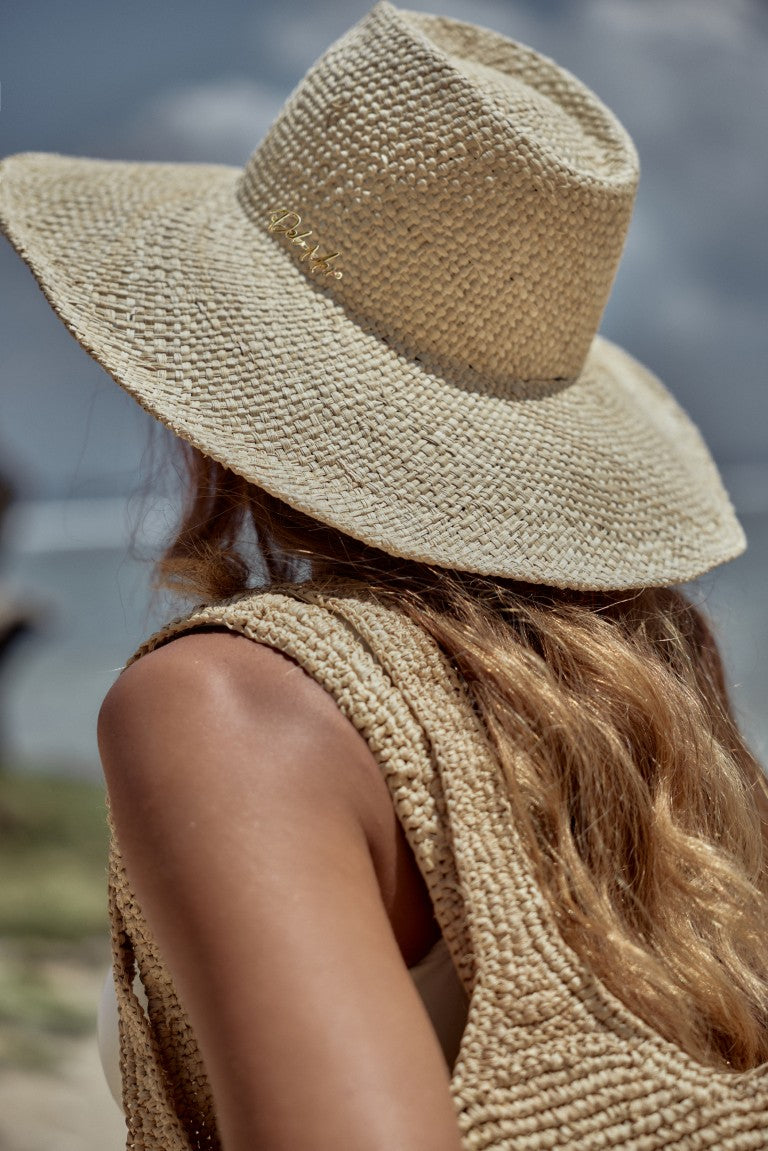Person wearing a straw hat and sleeveless top against a blurred natural background