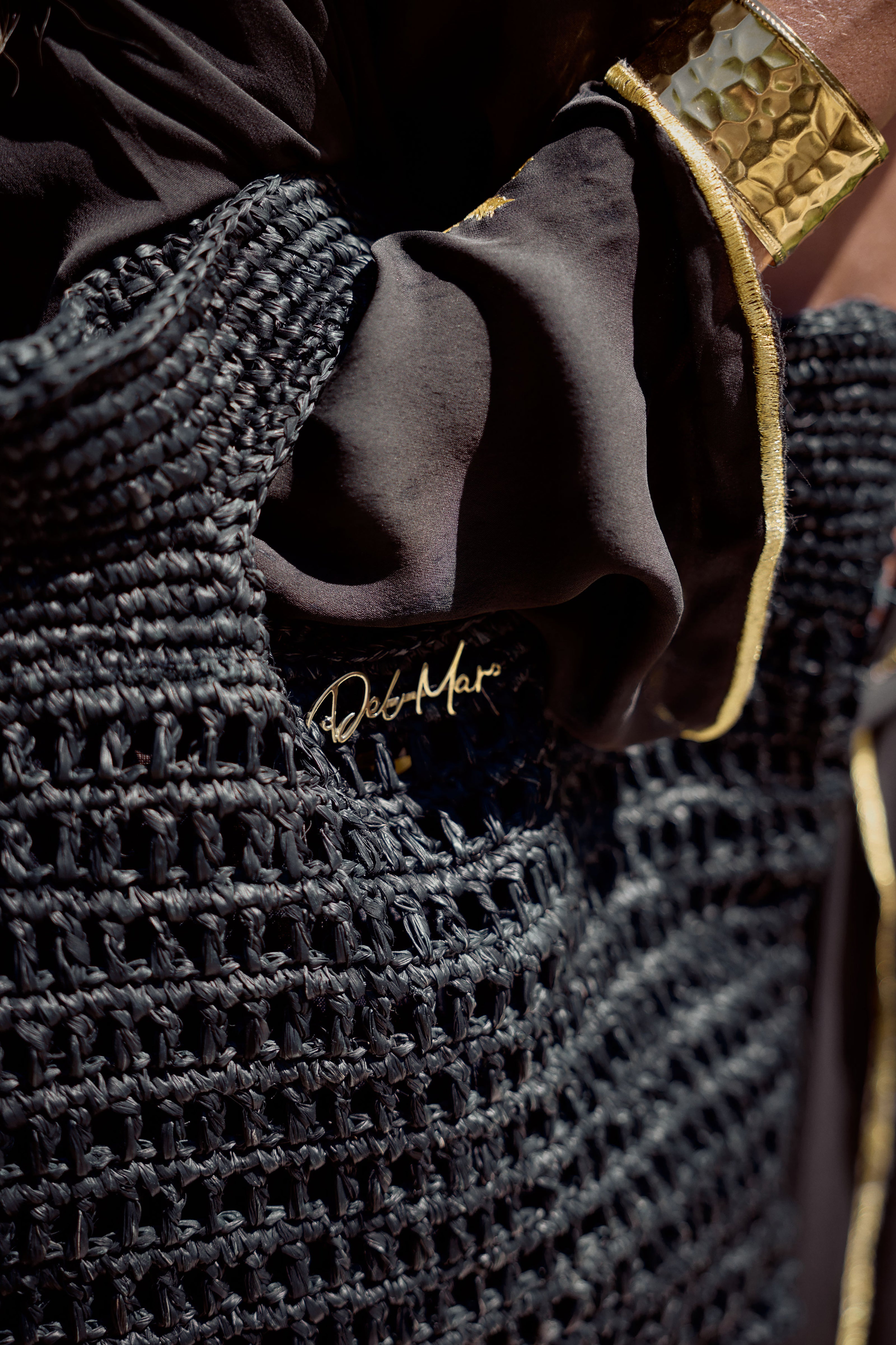 Close-up of a textured black woven bag with gold accents and a brand logo on