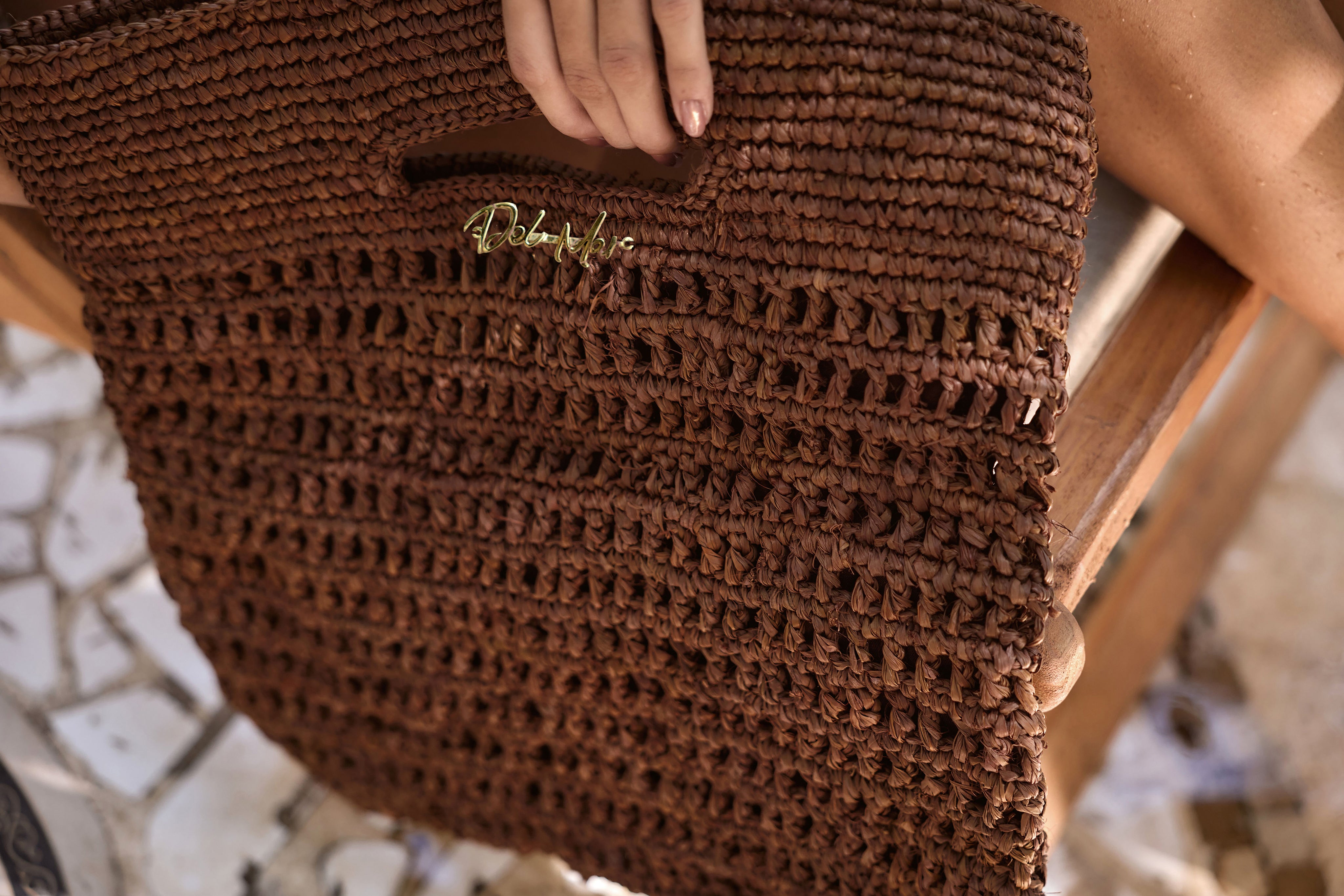Brown woven handbag with 'Del Mar' branding held by a person.