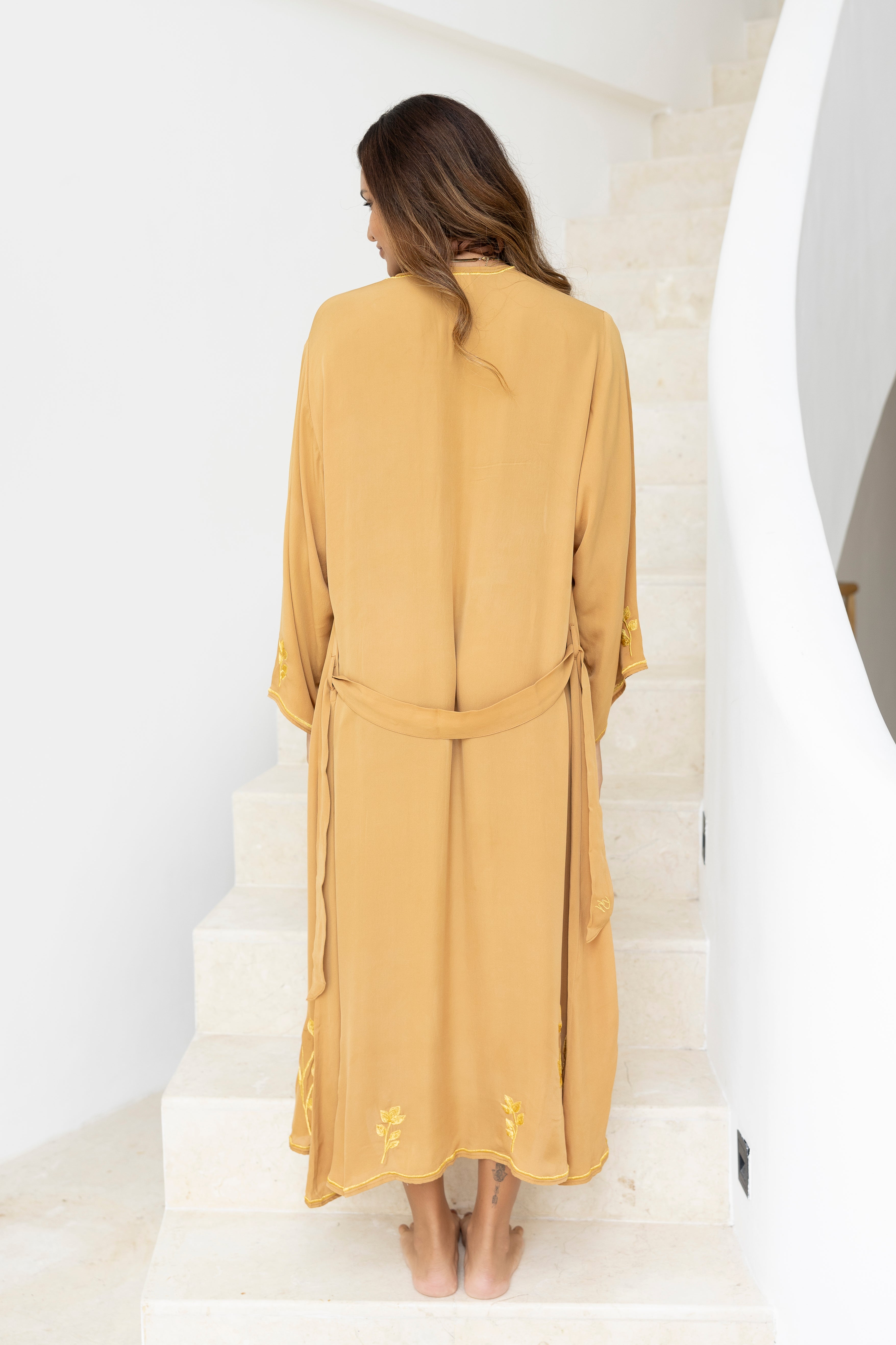 Woman in a taupe dress standing on white steps.