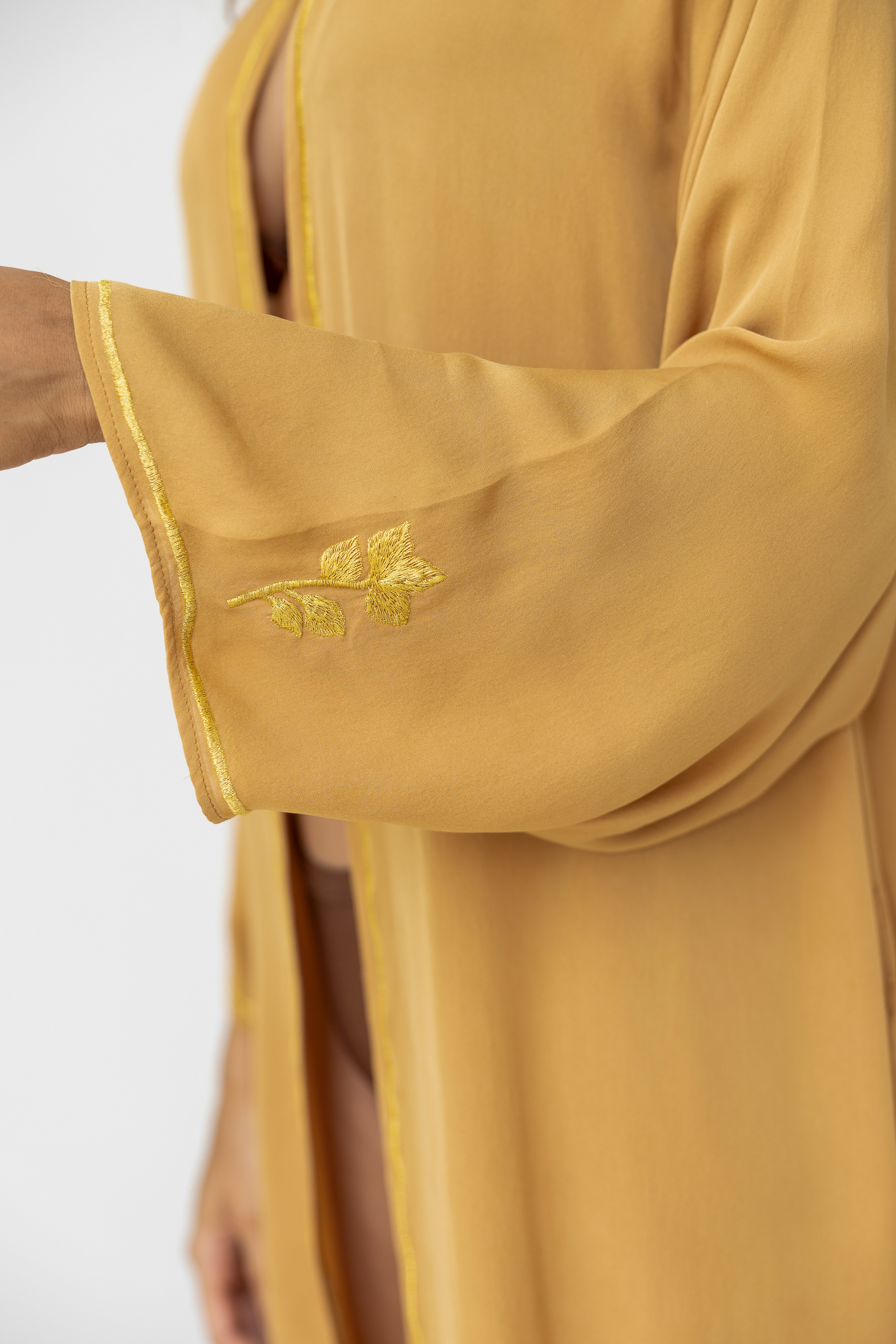 Close-up of a taupe garment with embroidered details on a white background